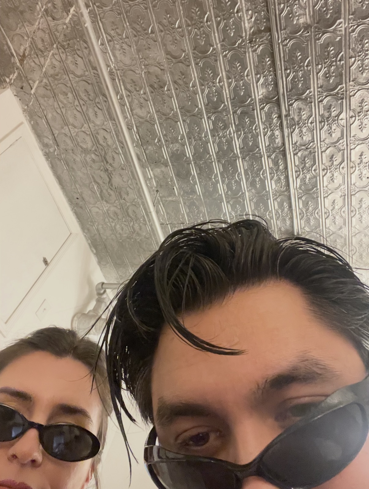 Kyle and Elise leaning close to the camera in sunglasses under a pressed-tin ceiling